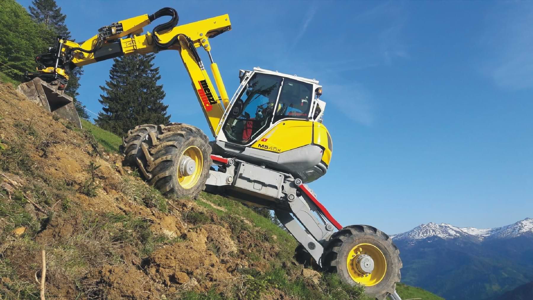 Ein gelber Teleskoplader, der auf einem steilen Hügel mit bergiger Kulisse arbeitet.